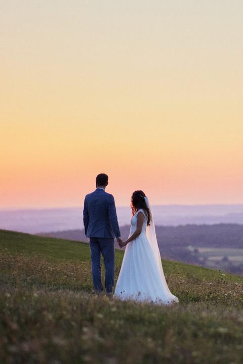 Brautpaar bei einem After-Wedding-Shooting auf einer Wiese im warmen Abendlicht mit Blick in die Ferne