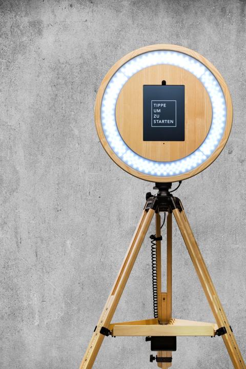 Lachendes Gästepaar mit Sonnenbrille und Hut vor einer hellen Fotobox-Wand auf einer Hochzeitsfeier