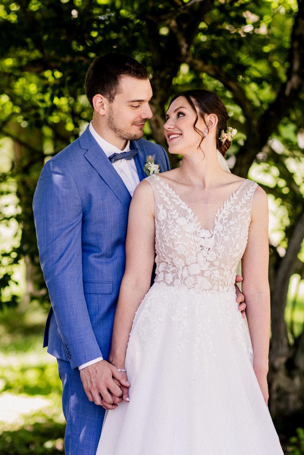 Brautpaar im Park blickt sich verliebt an, Braut im Spitzenkleid mit Blumen im Haar