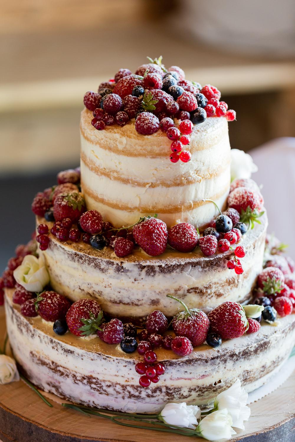 Dreistöckiger Naked Cake mit roten Beeren auf Holzbrett