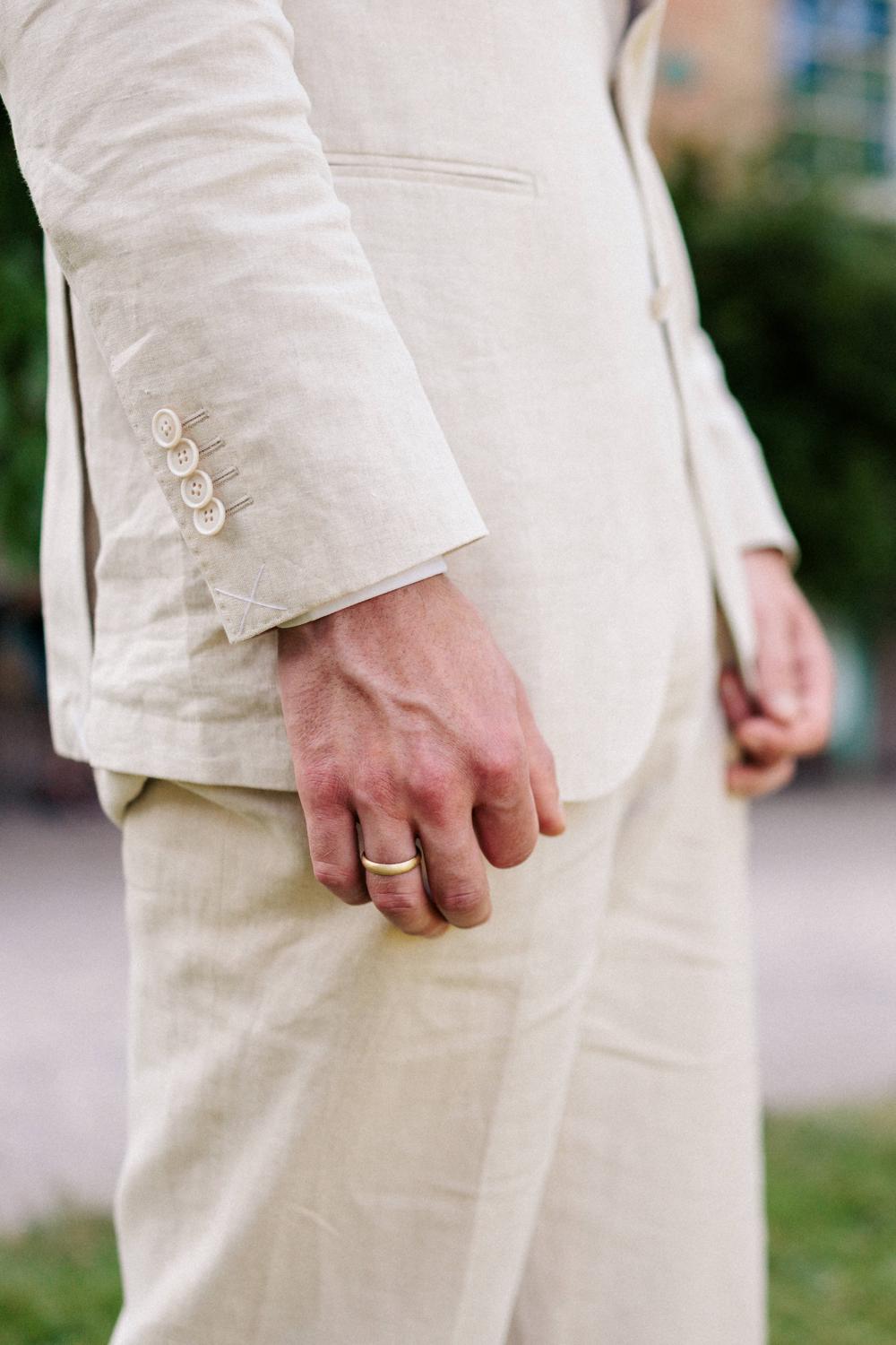 Detail: Hand des Bräutigams mit goldenem Ehering am Ärmel des hellen Leinenanzugs