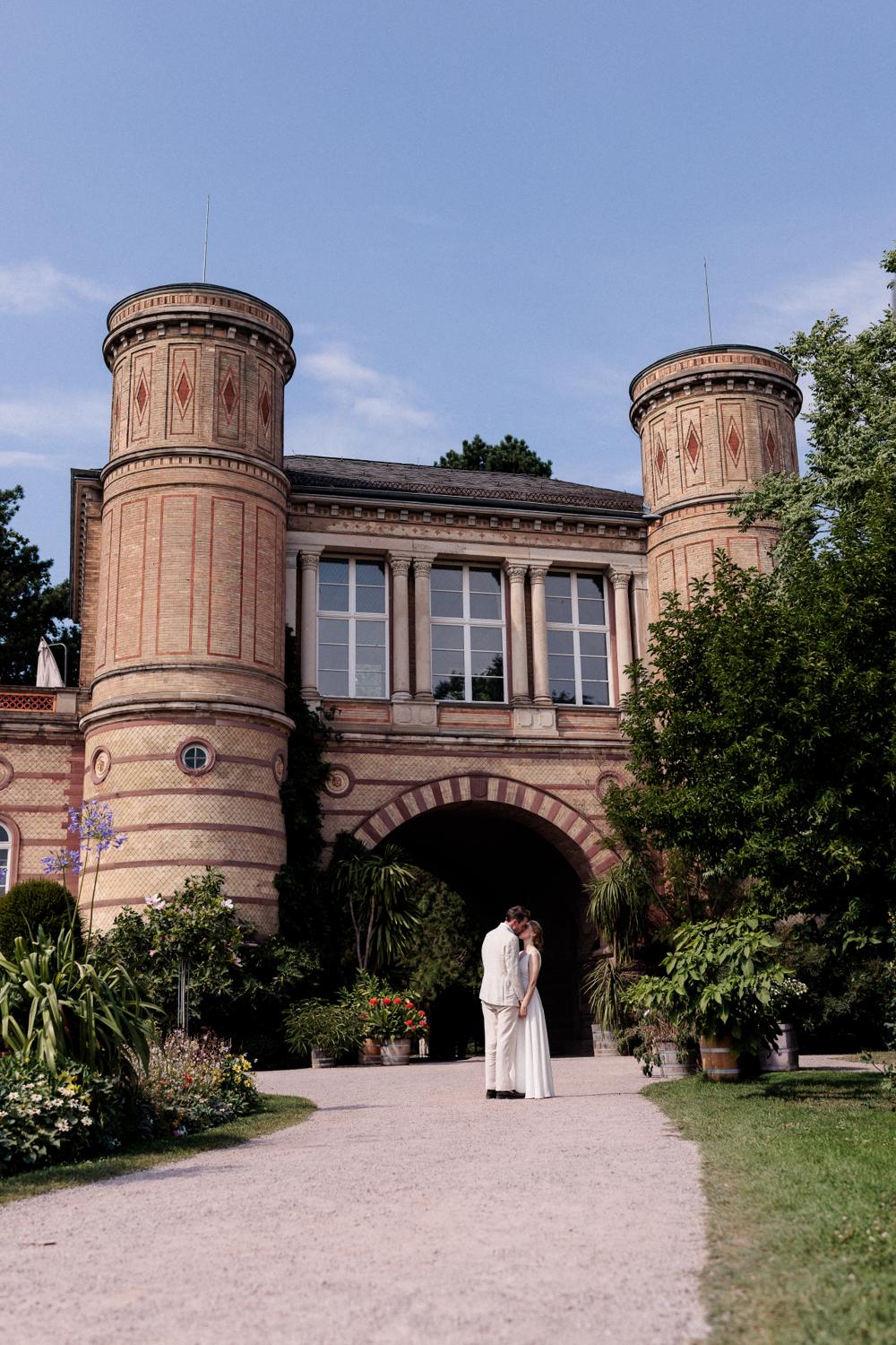 Brautpaar klein unter dem imposanten Torbogengebäude mit zwei Türmen im Botanischen Garten Karlsruhe