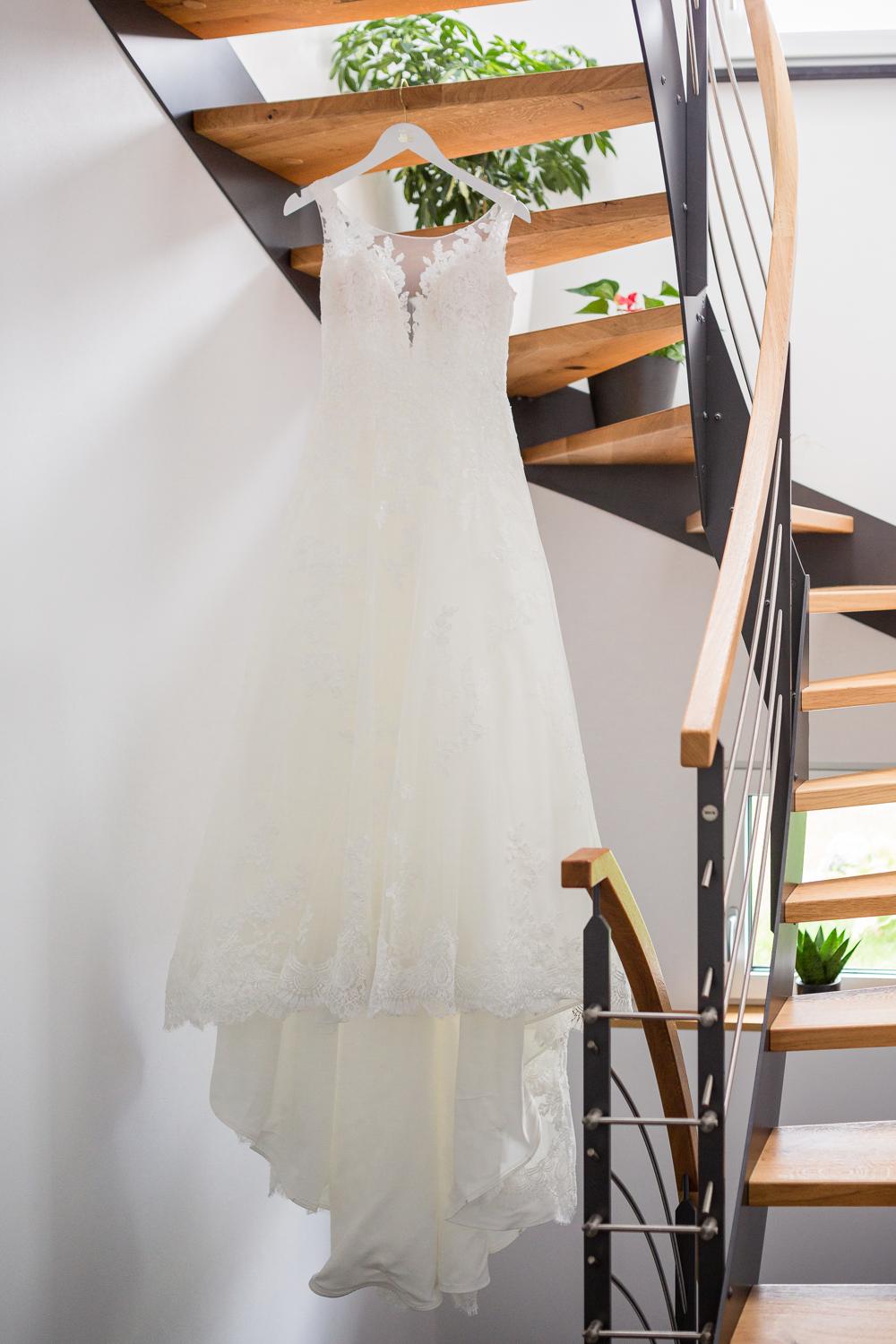 Brautkleid mit Spitze hängt an Holztreppe beim Getting Ready, Hochzeit Kloster Kirchberg