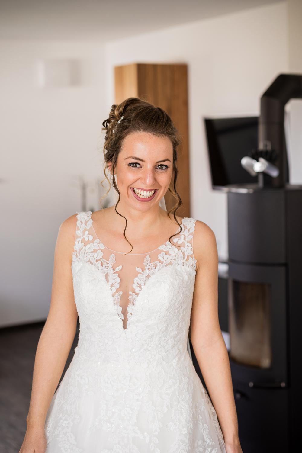 Braut lacht strahlend im Spitzenkleid mit tiefem V-Ausschnitt beim Getting Ready