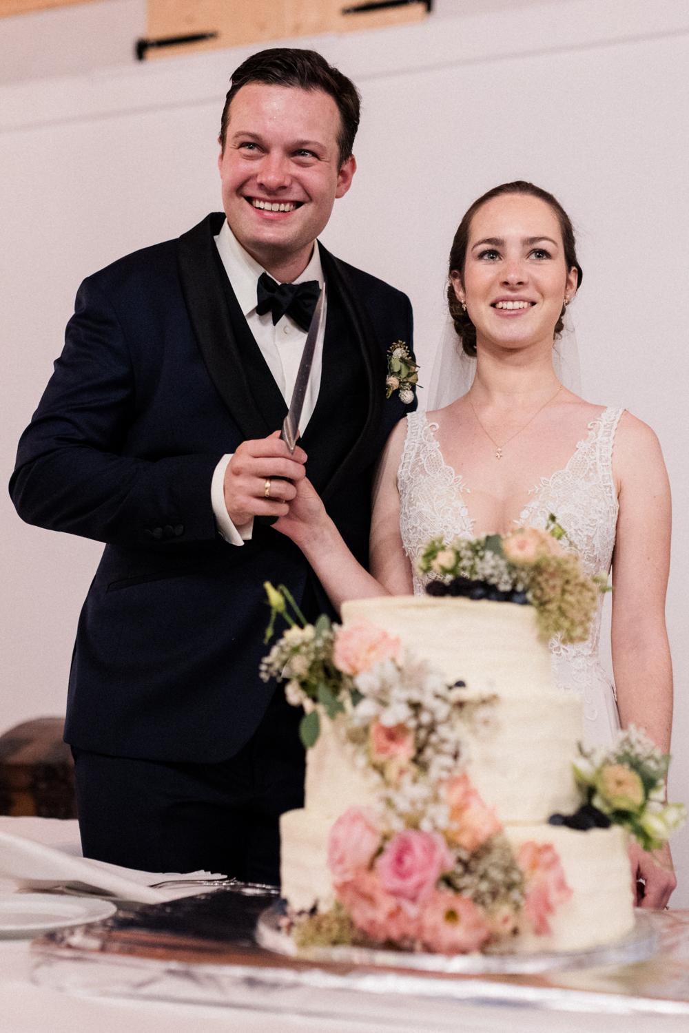 Brautpaar schneidet stolz die Hochzeitstorte mit Rosen an