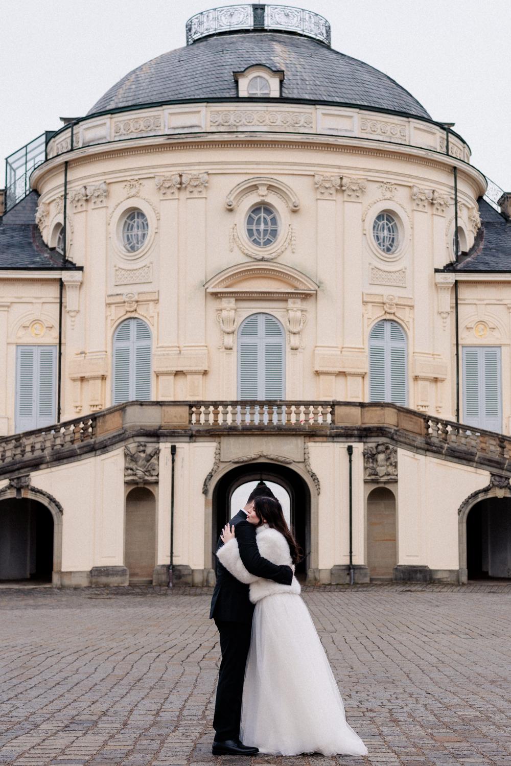 Brautpaar umarmt sich küssend unter einem Torbogen von Schloss Solitude in Stuttgart