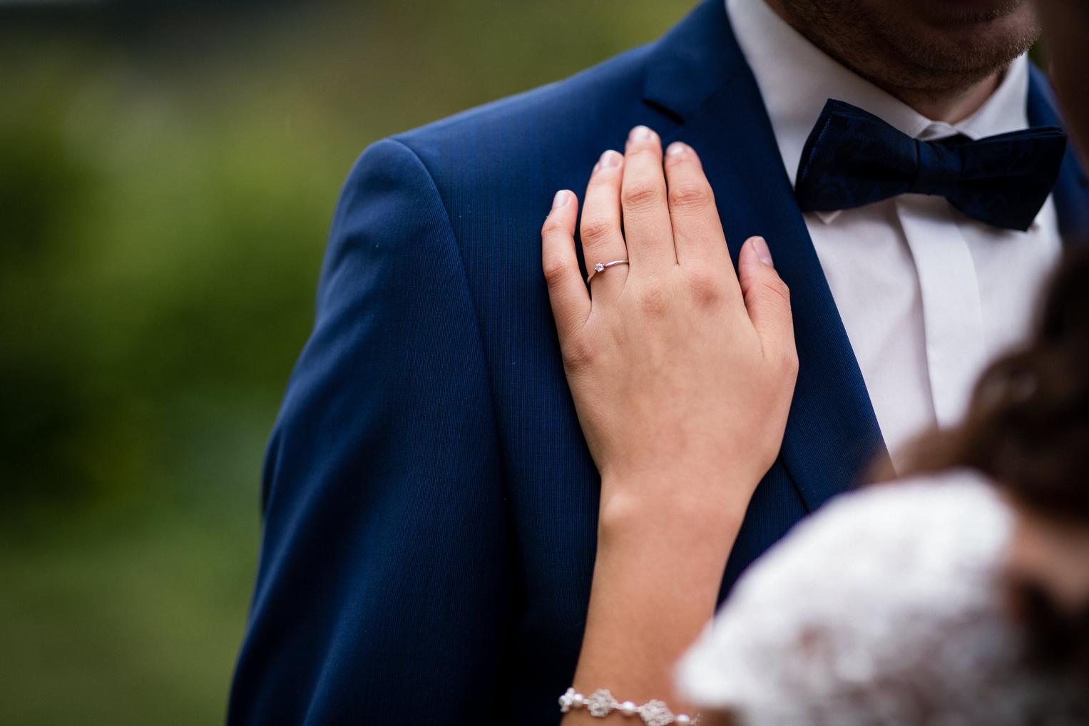 Nahaufnahme der Hand der Braut mit Verlobungsring auf dem Revers des Hochzeitsanzugs