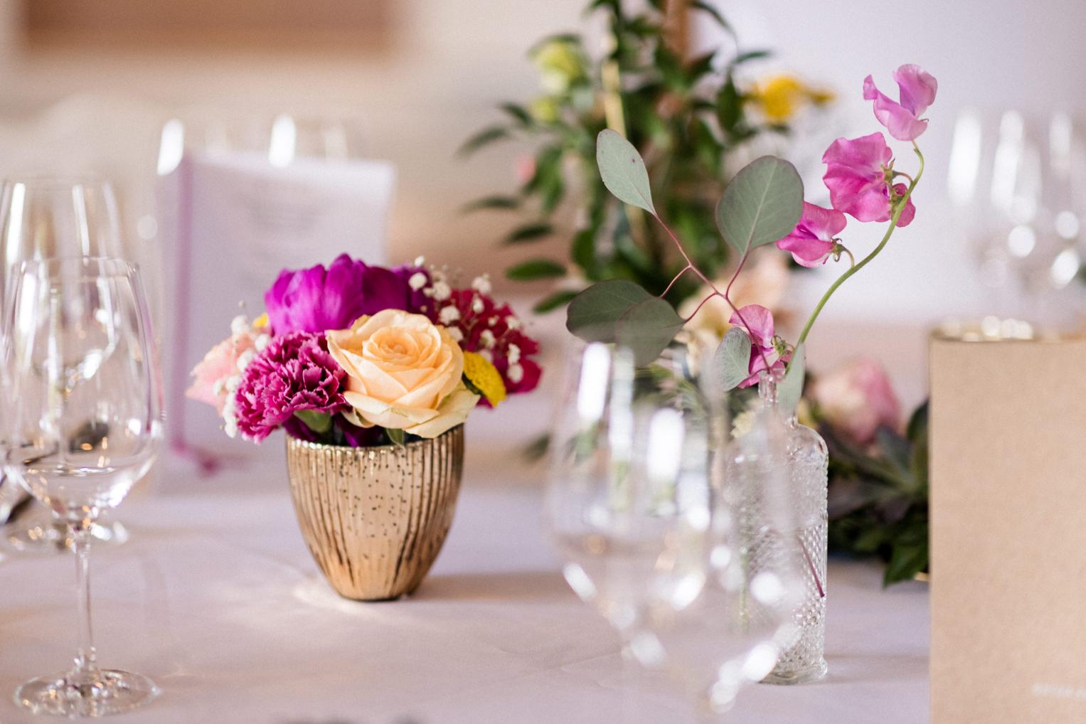 Nahaufnahme bunter Tischblumen in goldenen Vasen auf weißer Hochzeitstafel am Lindenhof