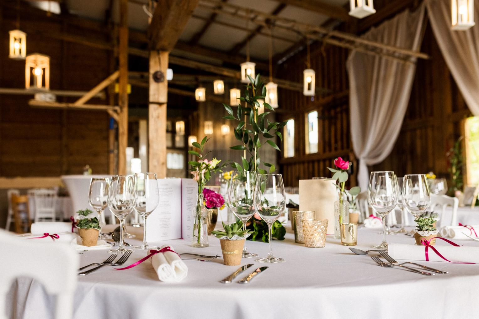 Vollständig gedeckter runder Hochzeitstisch mit Menükarte und Tischblumen in der Lindenhof-Scheune