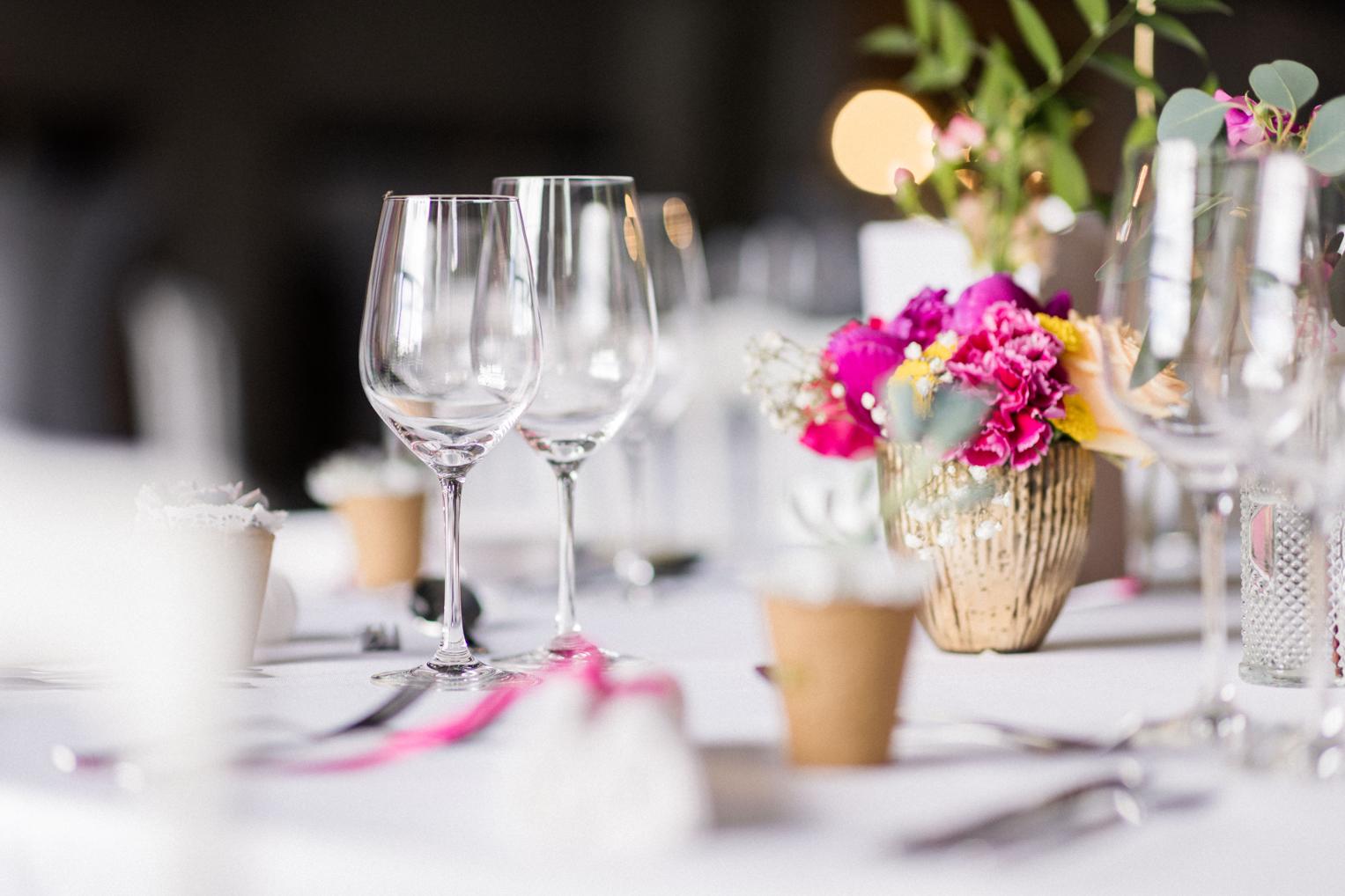 Detail: Weingläser und pinkes Blumenarrangement in Goldvase auf gedeckter Hochzeitstafel
