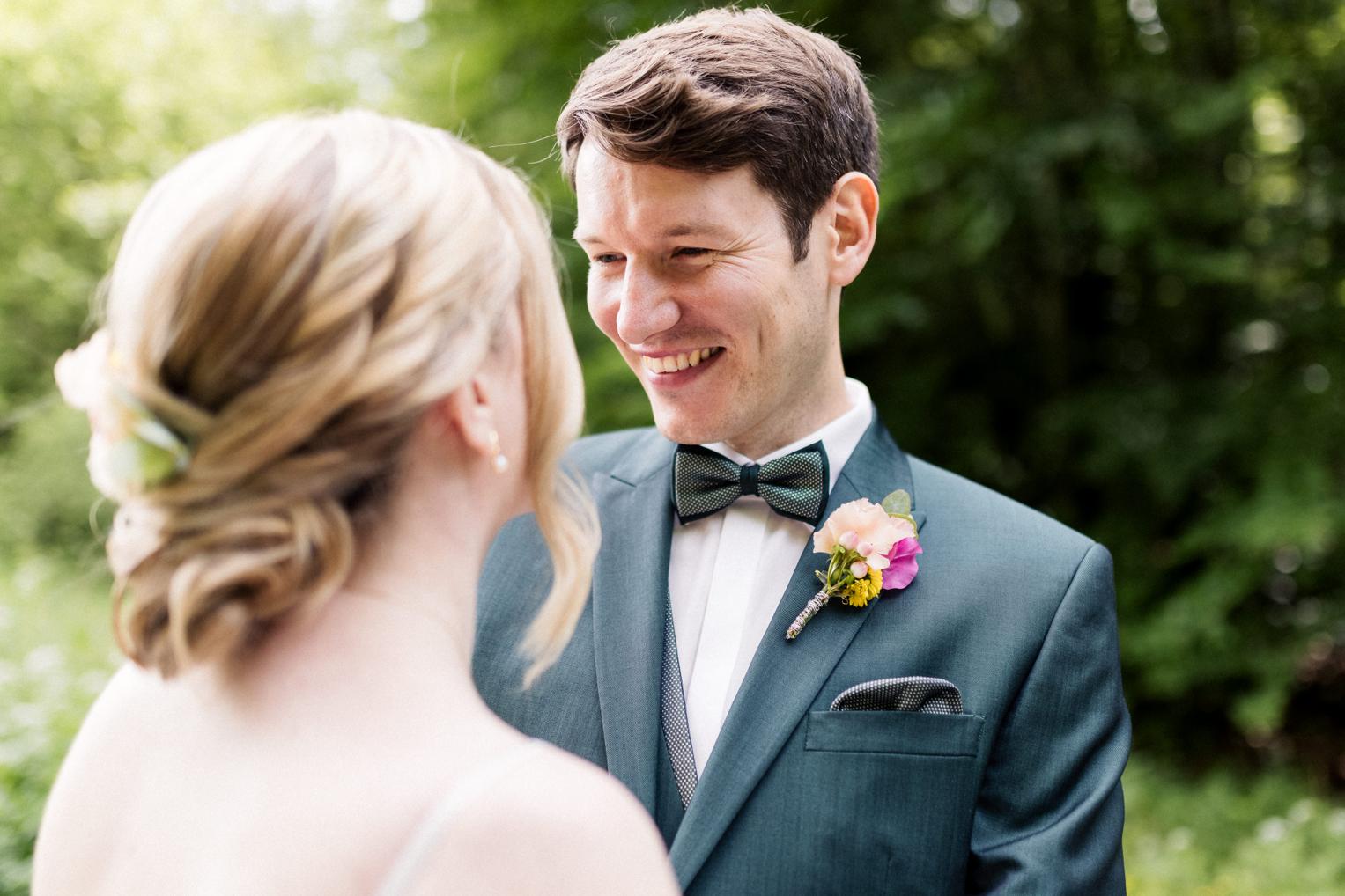 Bräutigam lächelt Braut an – Detail mit Fliege und Blumenboutonnière beim Shooting am Lindenhof