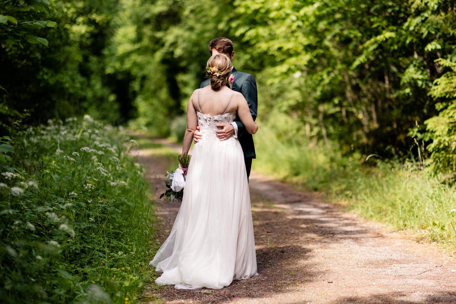 Brautpaar von hinten auf einem Feldweg – Brautkleid mit Schleppe, Brautstrauß, Lindenhof Mötzingen