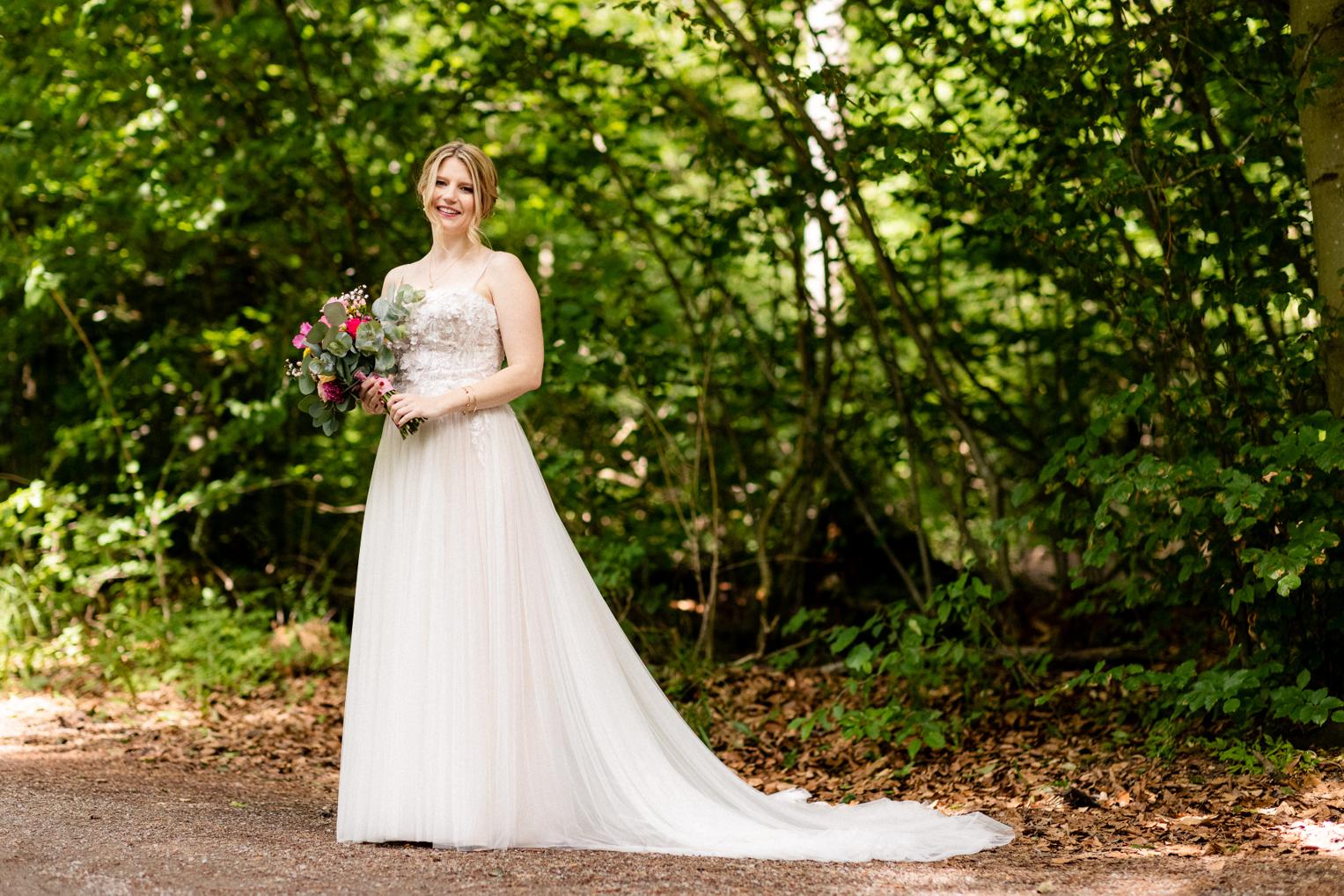 Braut im Tüllkleid mit buntem Brautstrauß aus Pfingstrosen und Rosen im Wald am Lindenhof