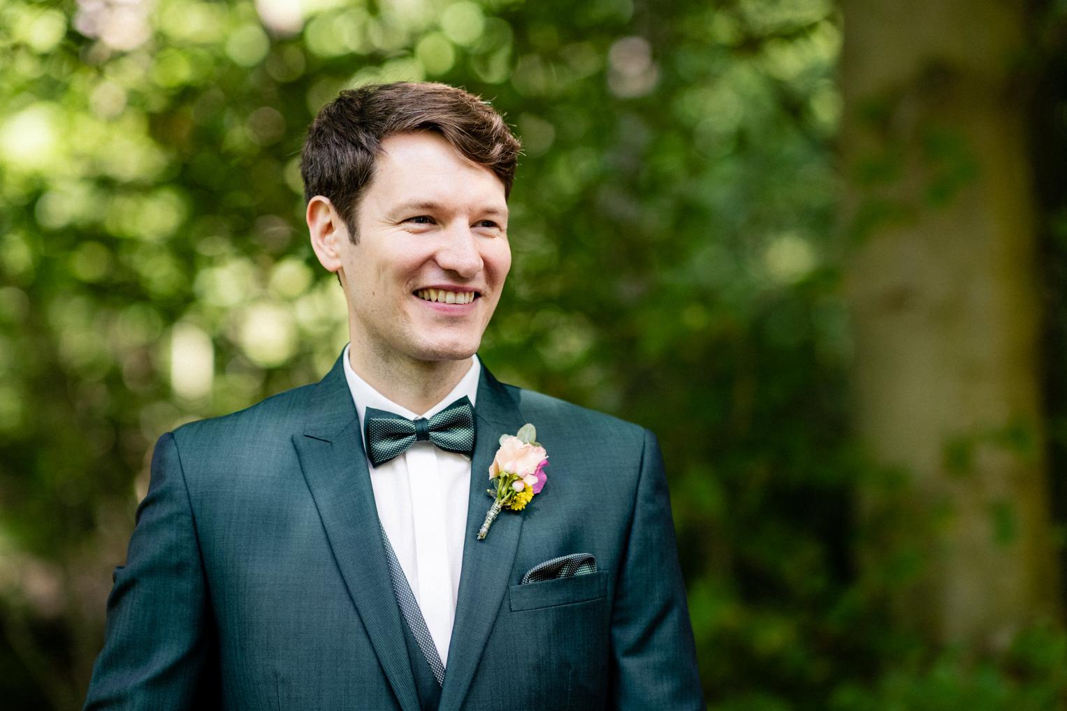 Bräutigam im dunkelgrünen Anzug mit Fliege und Boutonnière beim Paarshooting am Lindenhof