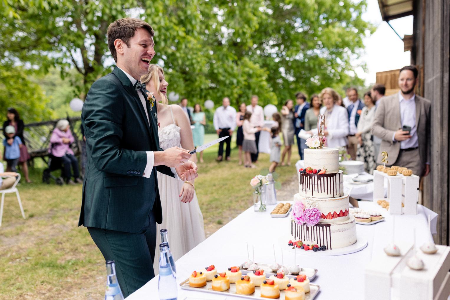 Brautpaar schneidet lachend die Hochzeitstorte am Sweet Table im Garten des Lindenhof Mötzingen an