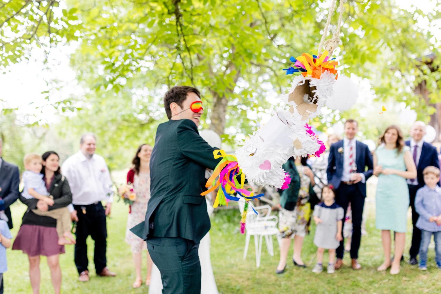 Bräutigam trifft die Piñata beim ausgelassenen Spiel mit Gästen im Freien am Lindenhof Mötzingen