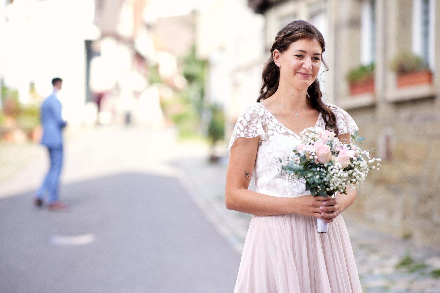 Braut mit Blumenstrauß während eines First-Look-Shootings in der Altstadt von Herrenberg, Bräutigam im Hintergrund.
