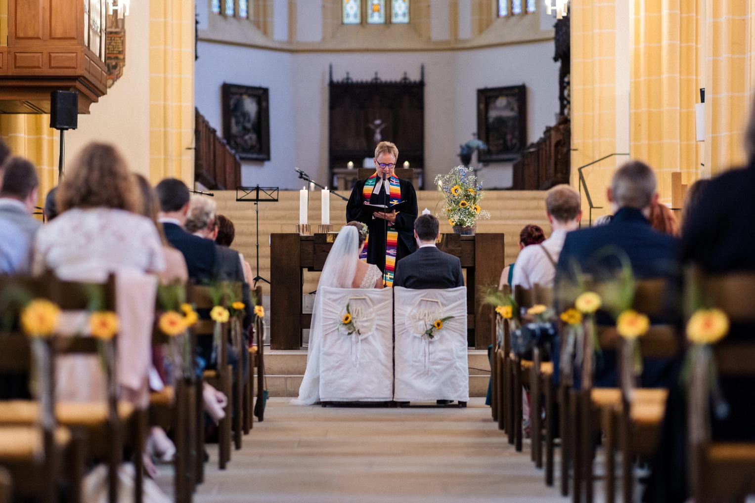 Brautpaar sitzt während der Zeremonie vor dem Altar der Stiftskirche in Herrenberg, während der Pfarrer spricht.