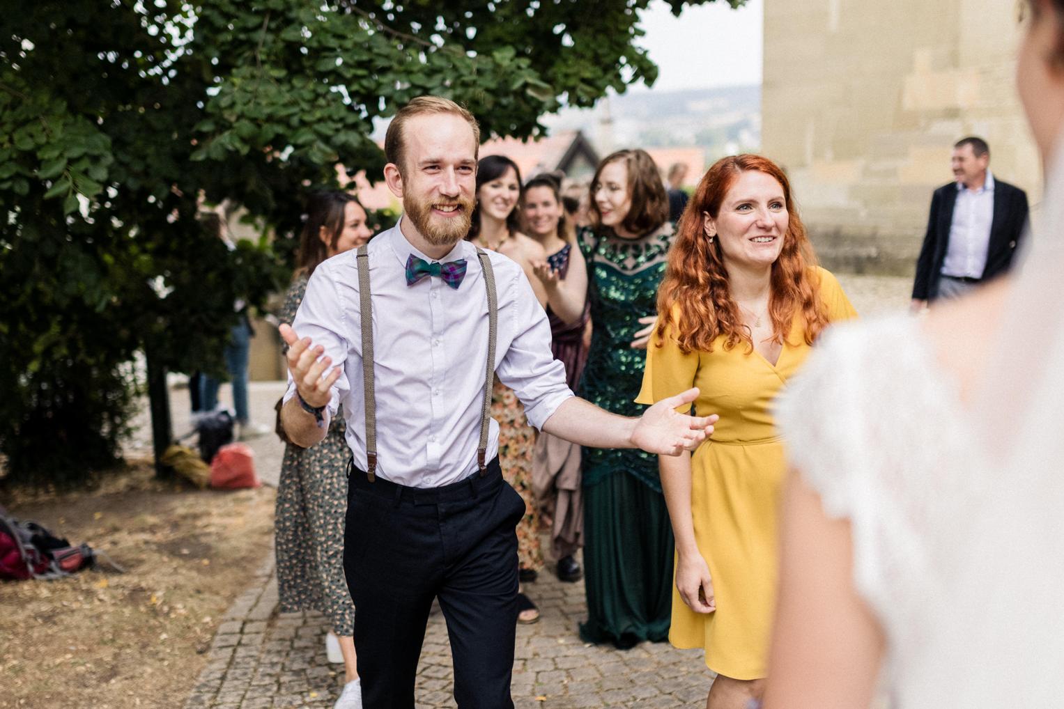 Gratulanten stehen vor der Stiftskirche Herrenberg, während ein Gast die Braut mit offenen Armen begrüßt.