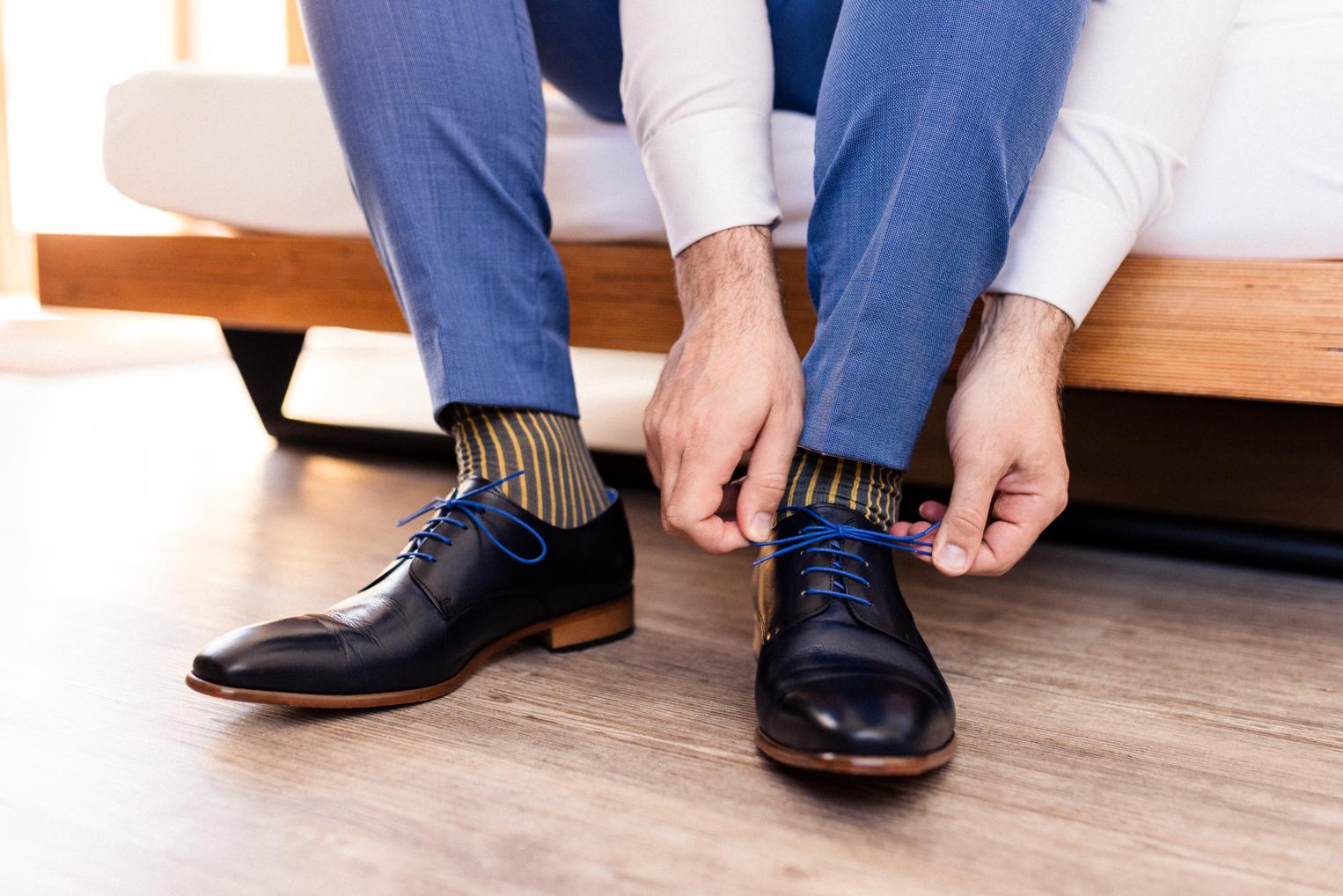 Bräutigam bindet seine dunkelblauen Lederschuhe mit blauen Schnürsenkeln, gestreifte Socken