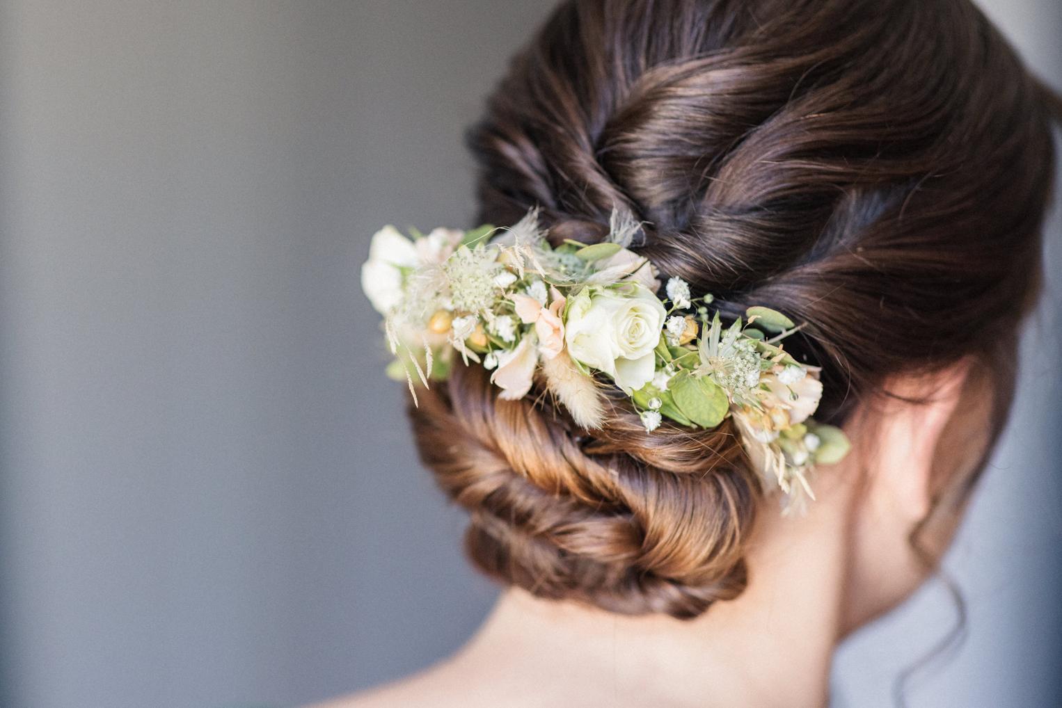 Hochsteckfrisur der Braut mit zartem Blumenschmuck in Creme und Grün, Detail von hinten