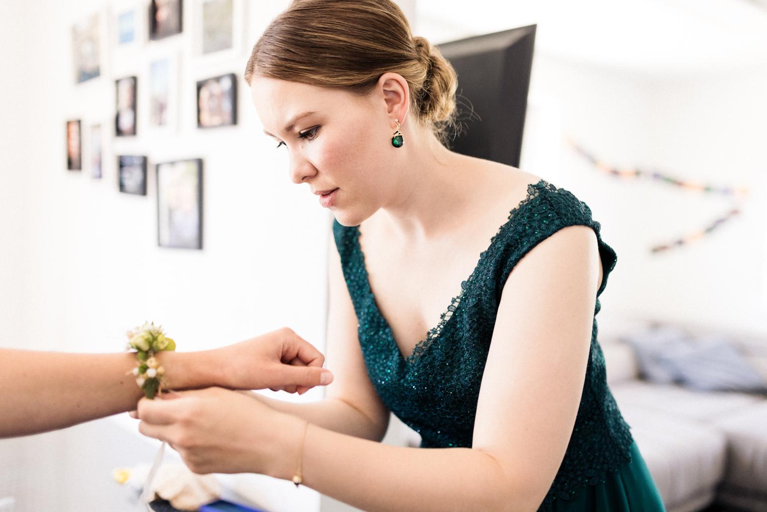 Brautjungfer in grünem Pailettenkleid bindet konzentriert ein Blumenarmband