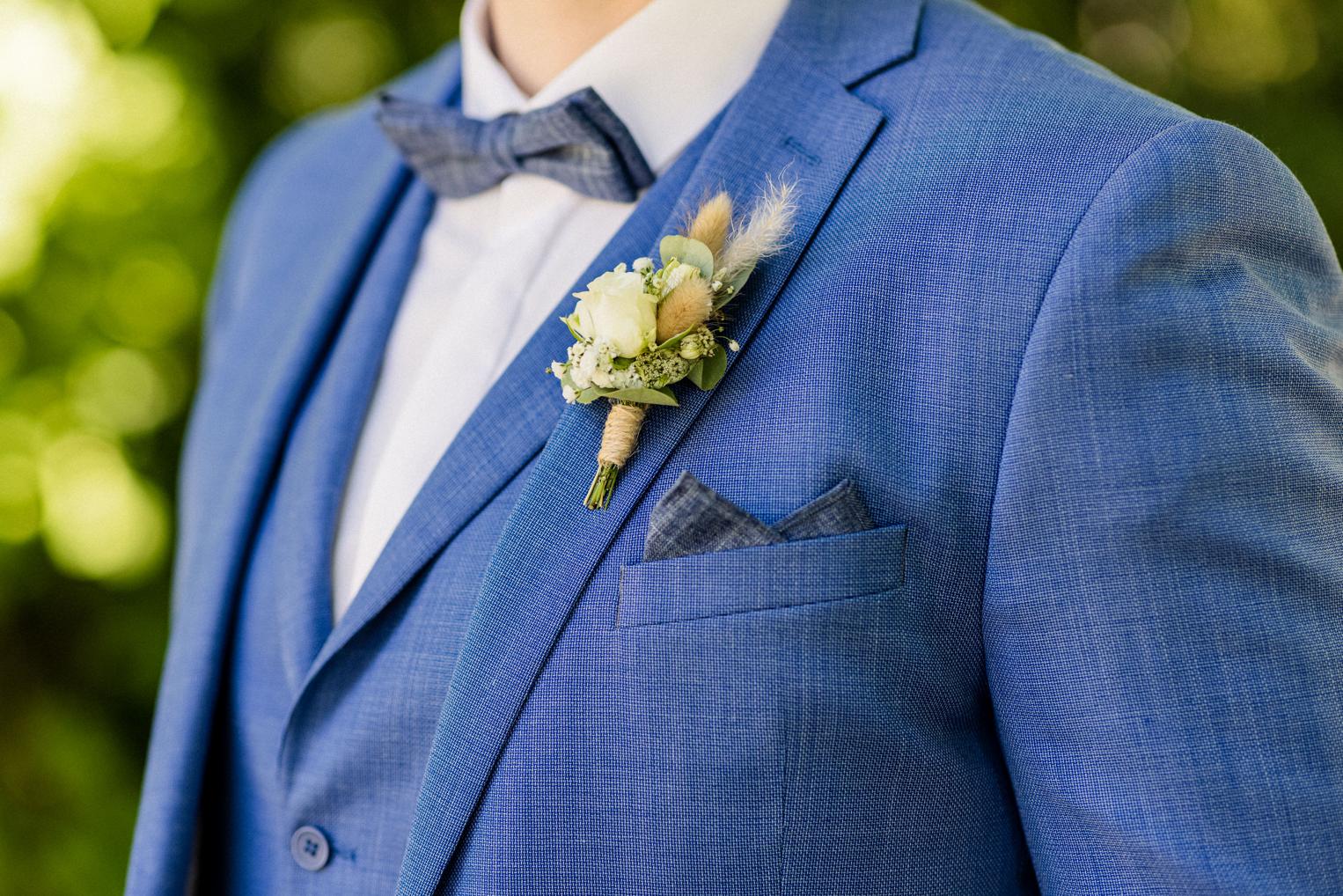 Detail – blaue Fliege und Ansteckblume mit weißen Blüten am hellblauen Anzug des Bräutigams