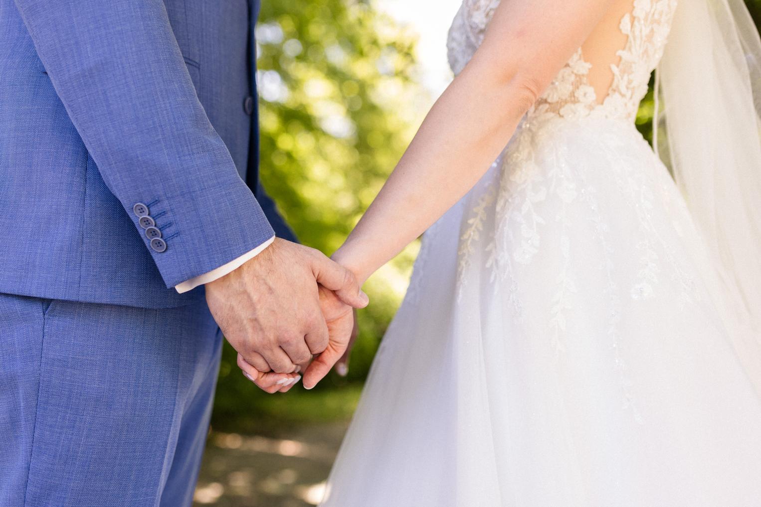 Brautpaar Hand in Hand, Detail von Spitzenkleid und hellblauem Anzug im Park