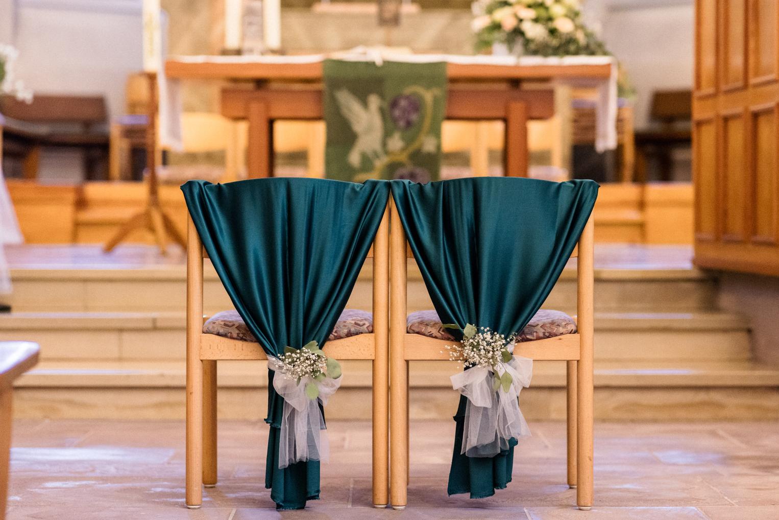 Zwei Stühle für das Brautpaar mit dunkelgrünem Stoff und Blumenschmuck vor dem Altar