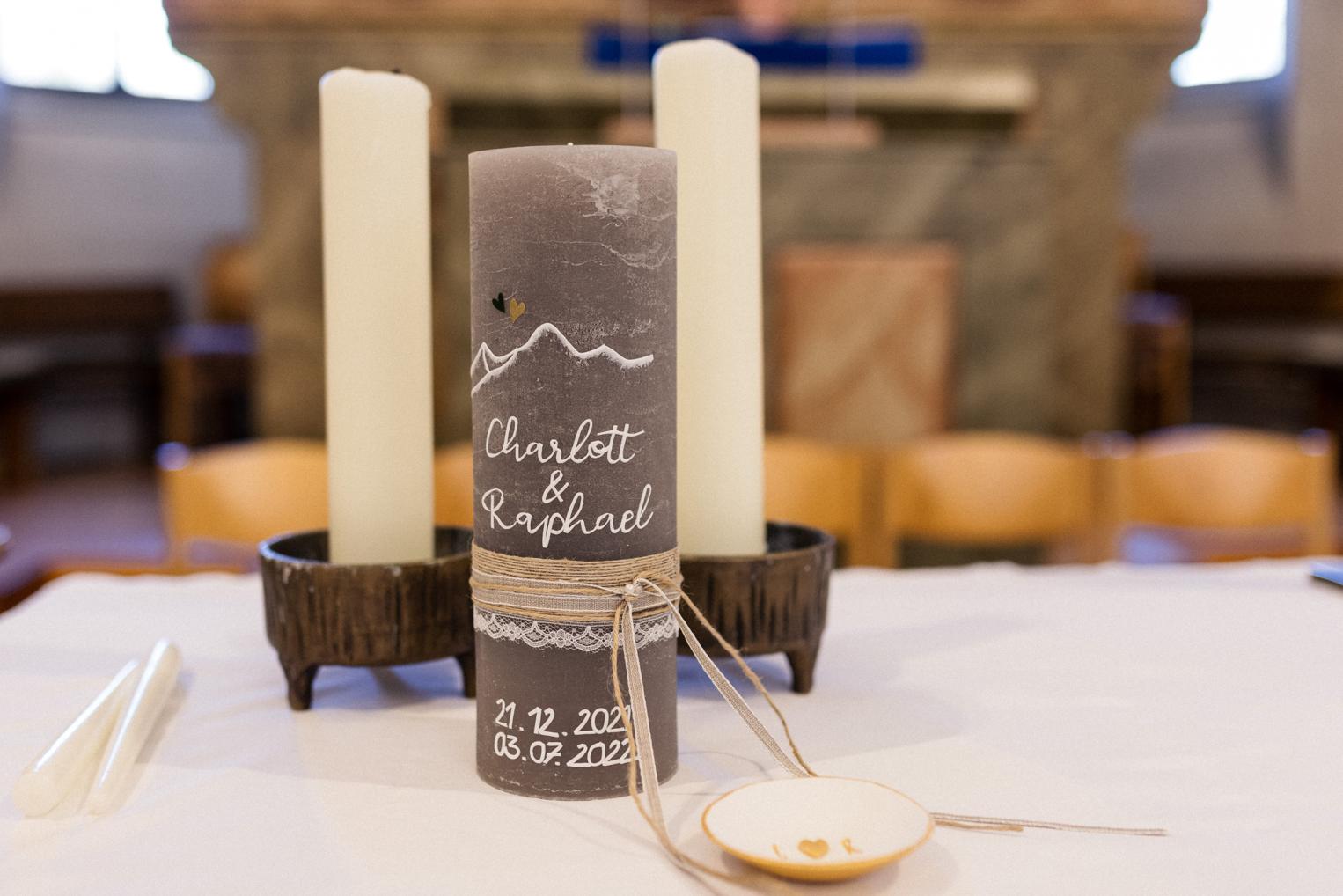 Hochzeitskerze des Brautpaares mit Bergmotiv und Spitze zwischen zwei weißen Kerzen auf dem Altar