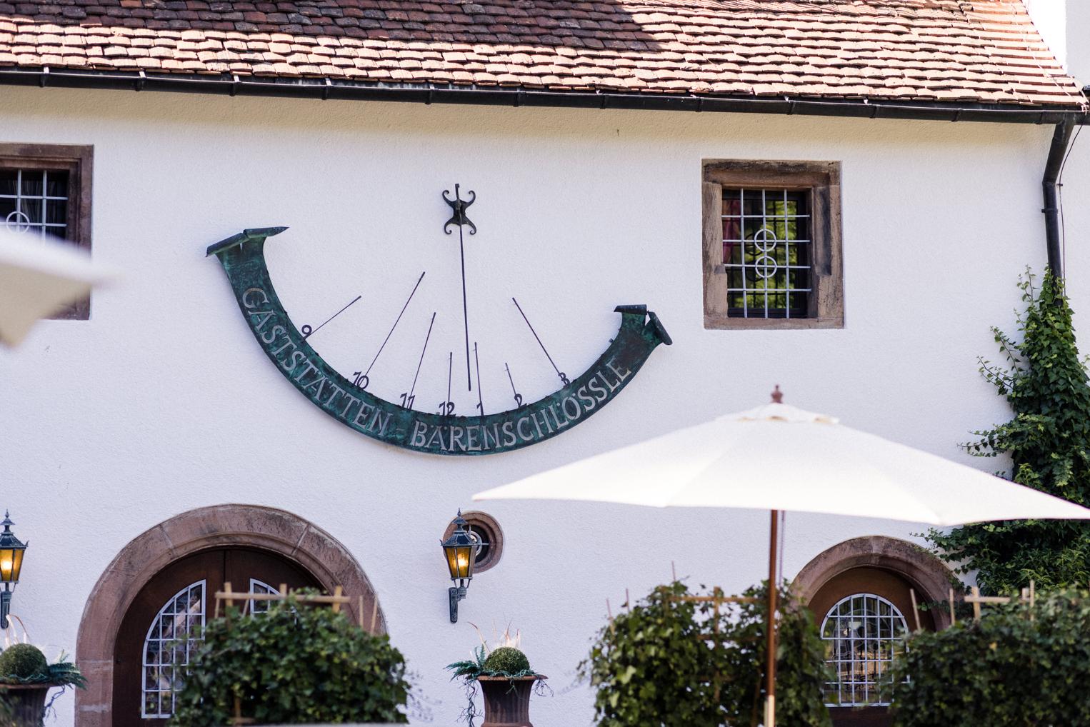 Sonnenuhr mit Schriftzug Gaststätten Bärenschlössle an der weißen Fassade des Hofguts, Rundbogentüren