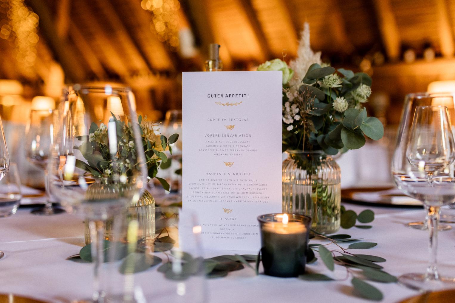 Menükarte Guten Appetit zwischen Blumen, Kerzen und Eukalyptus auf dem Hochzeitstisch