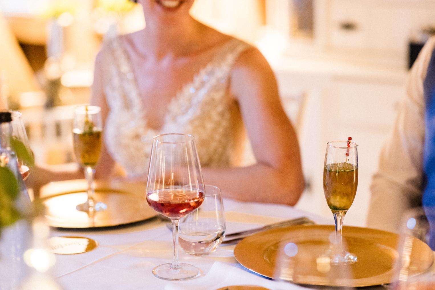 Braut am Tisch mit Sekt- und Weingläsern auf goldenen Platztellern, Detail im warmen Licht