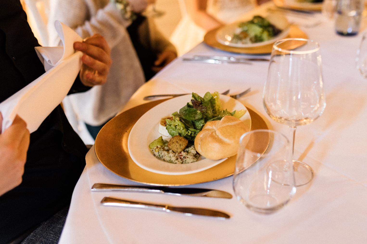 Vorspeise auf goldenem Platzteller wird serviert – Salat mit Brötchen auf der Hochzeitstafel
