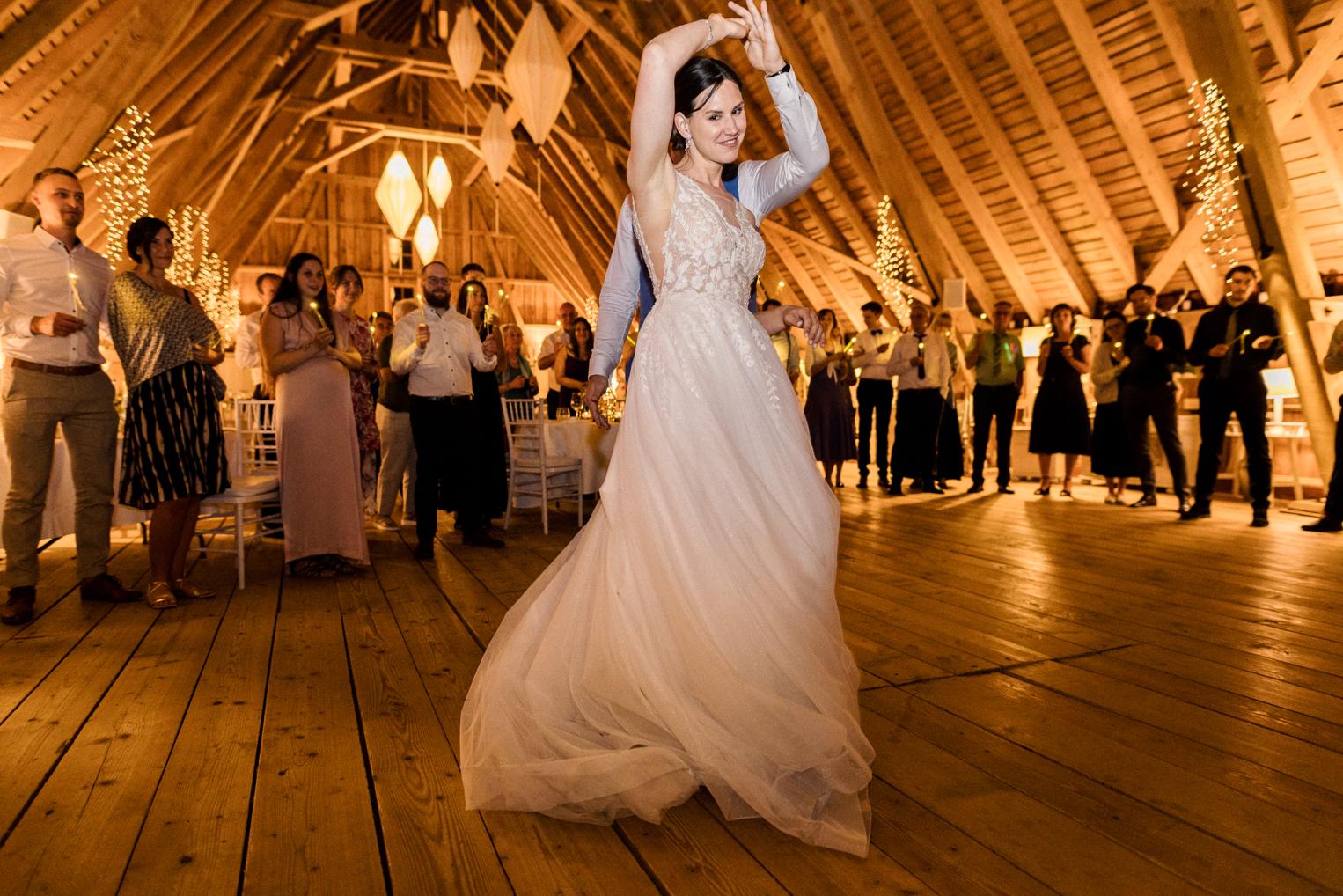 Braut wirbelt beim Hochzeitstanz, Tüllrock schwingt unter dem Holzgebälk der Scheune