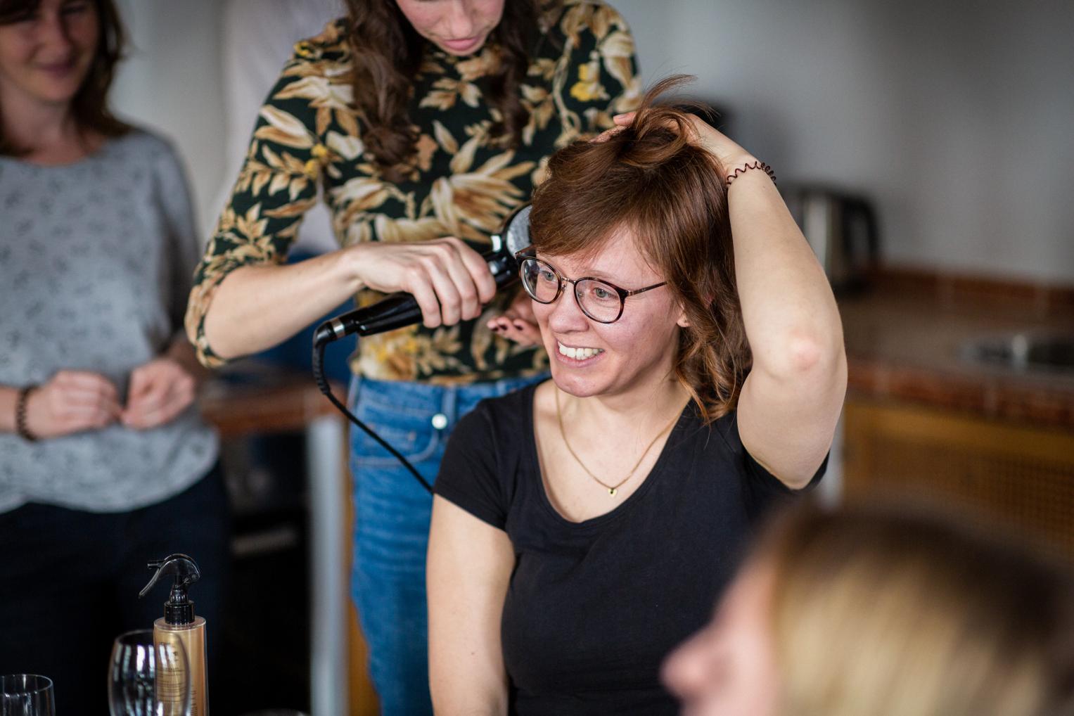 Braut lacht beim Haarstyling mit Lockenstab im Getting Ready