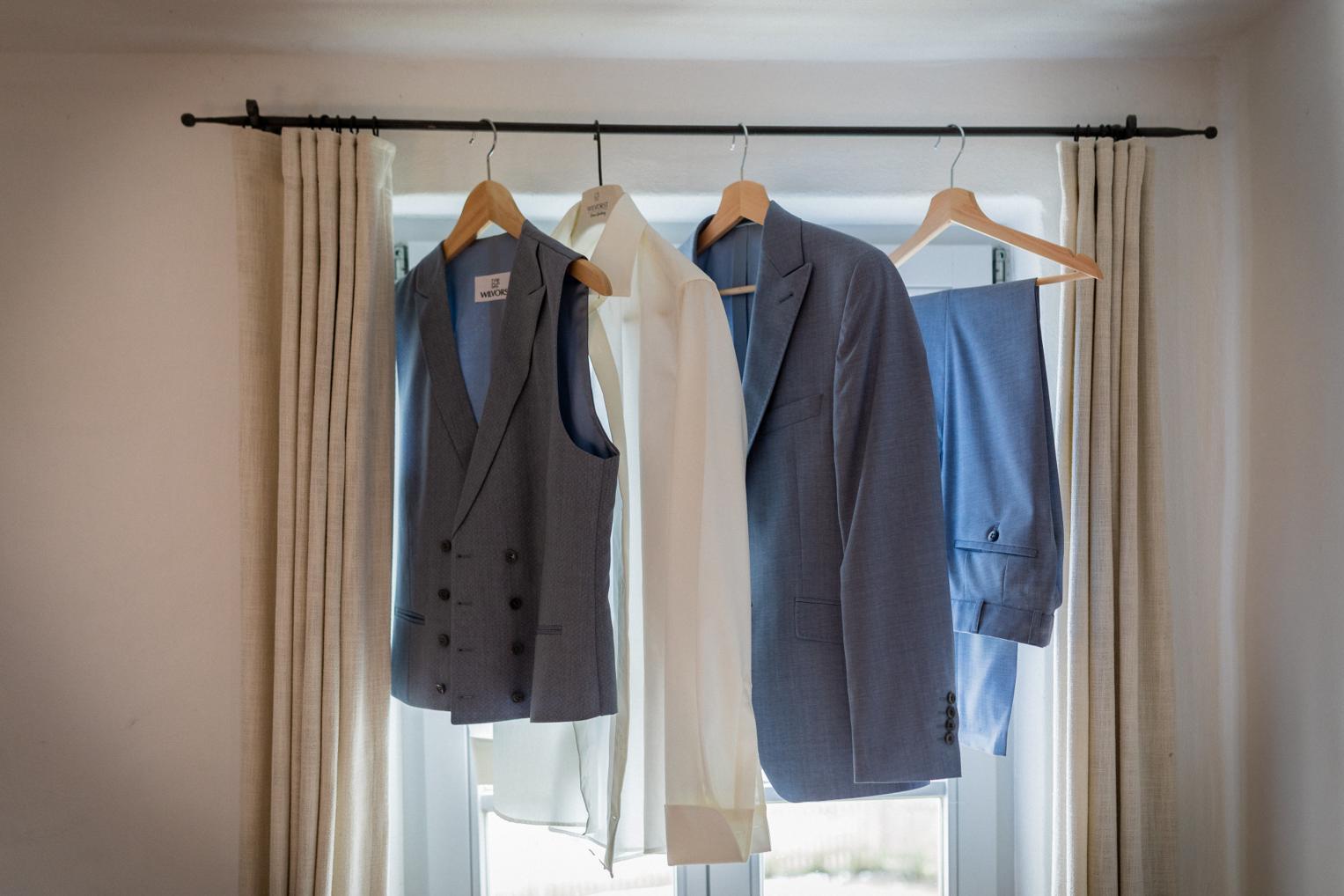 Hellblauer Anzug des Bräutigams mit Weste hängt am Fenster