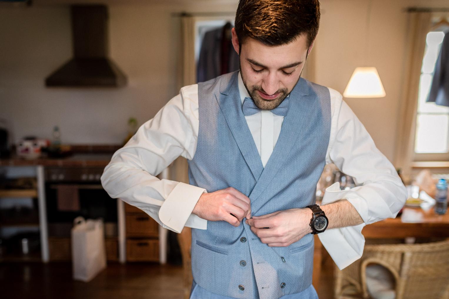 Bräutigam knöpft seine hellblaue Weste vor der Hochzeit zu