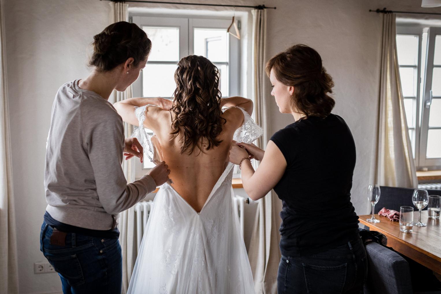 Freundinnen helfen der Braut in ihr Spitzenkleid