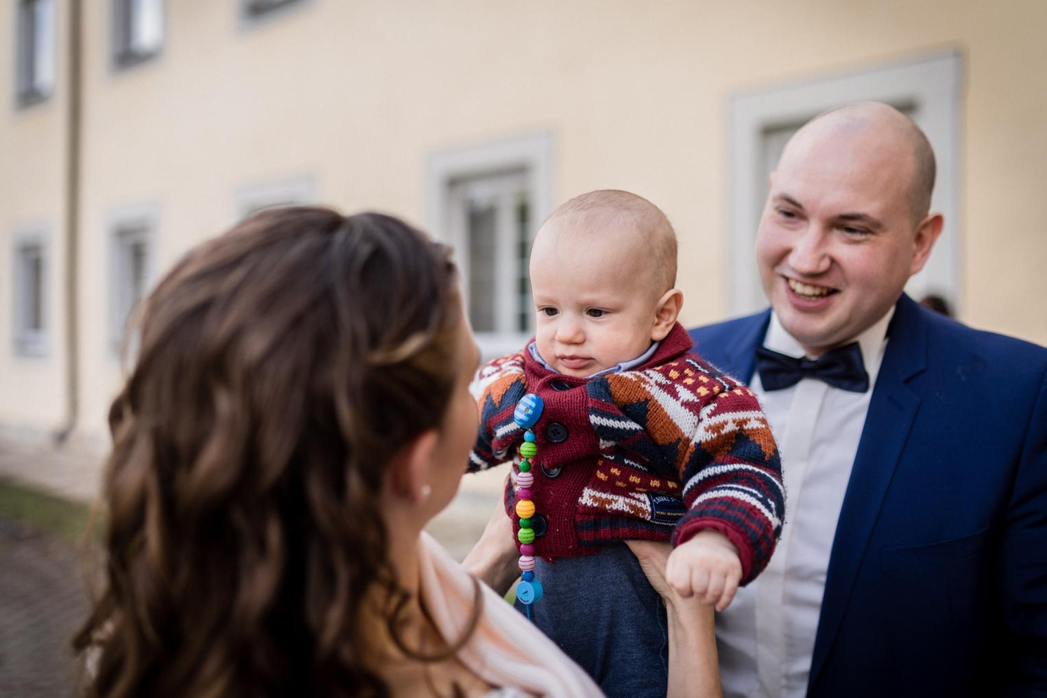 Bräutigam mit Baby auf dem Arm beim Sektempfang am Kloster