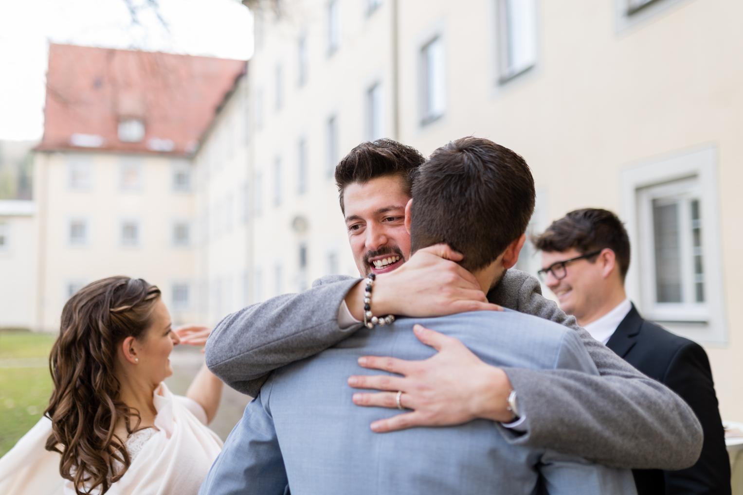 Bräutigam umarmt seinen Trauzeugen vor dem Kloster
