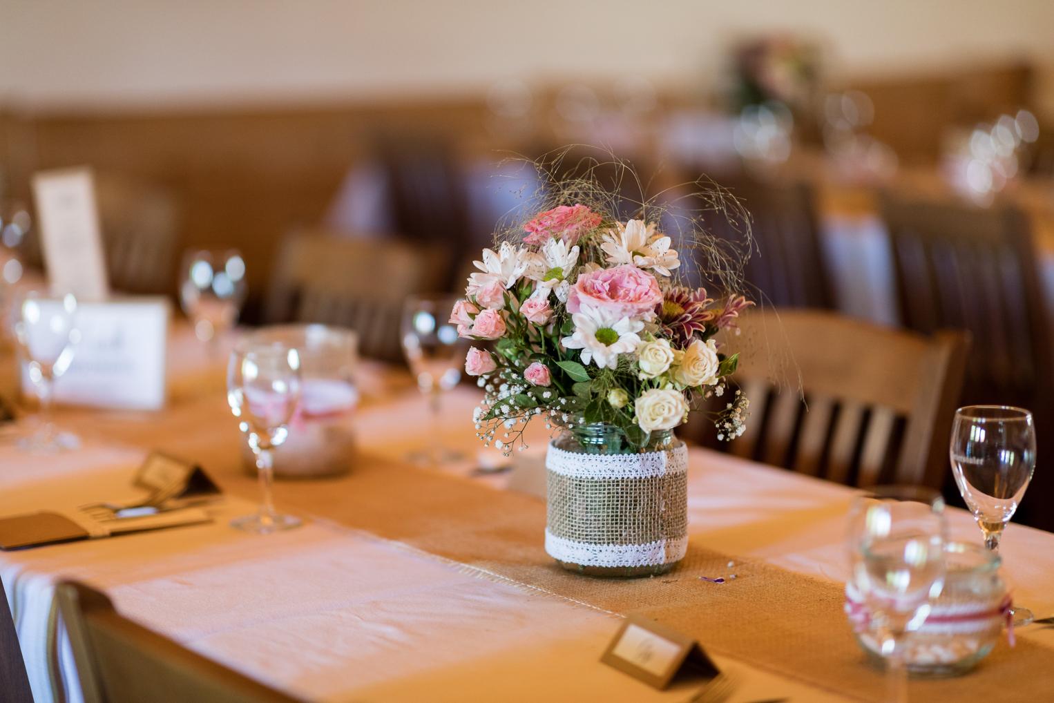 Tischdetail mit rosa Blumen in Glasvase und Jutemanschette