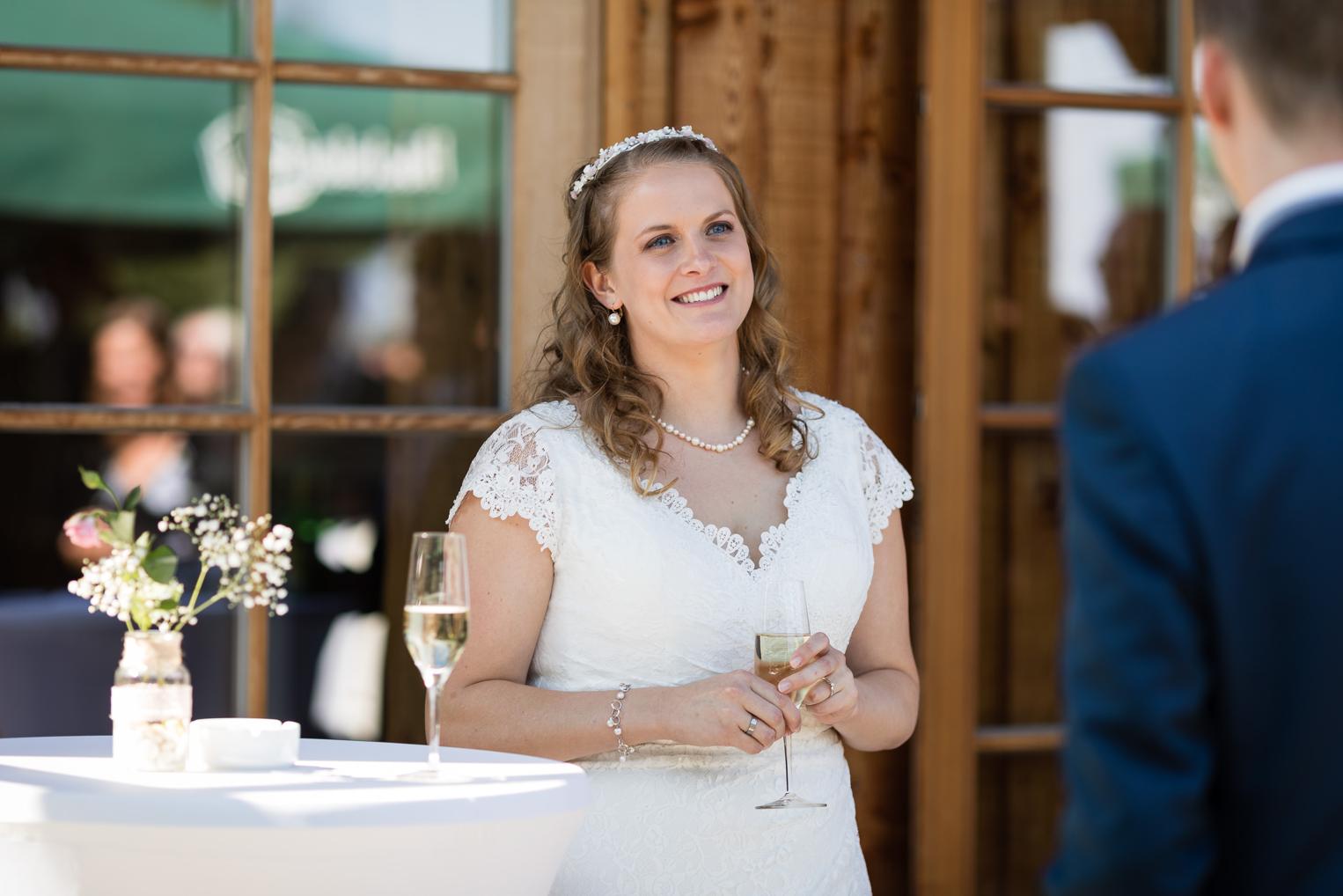 Braut mit Tiara und Spitzenkleid beim Sektempfang