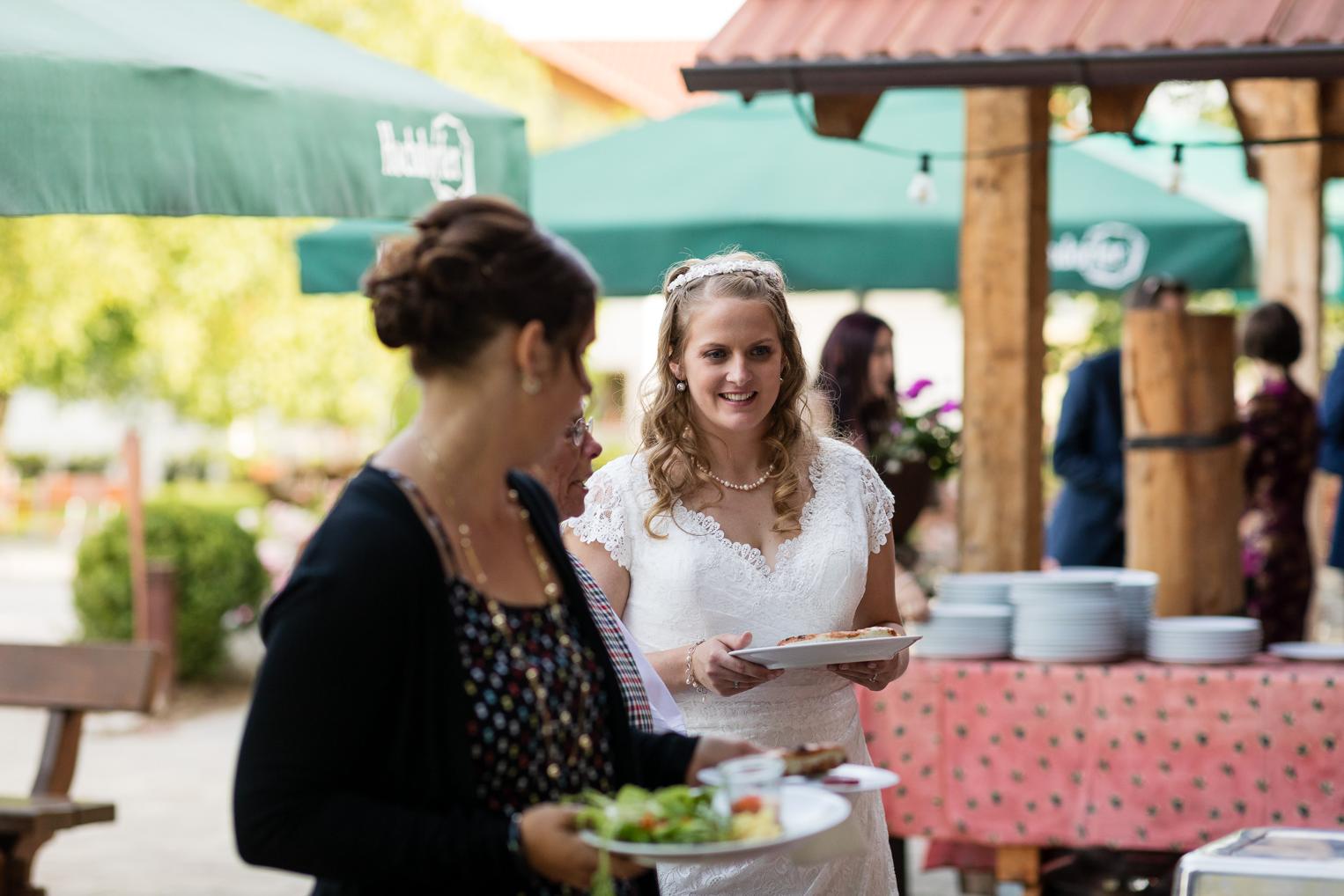 Braut holt sich lachend Essen am Grillbuffet
