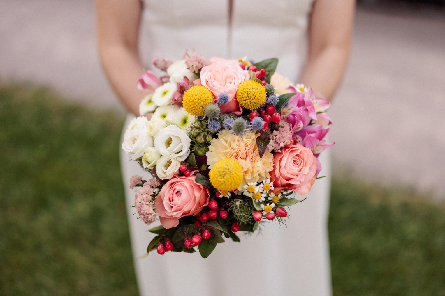 Farbenfroher Brautstrauß mit Rosen und Wiesenblumen, von der Braut vor dem Kleid gehalten
