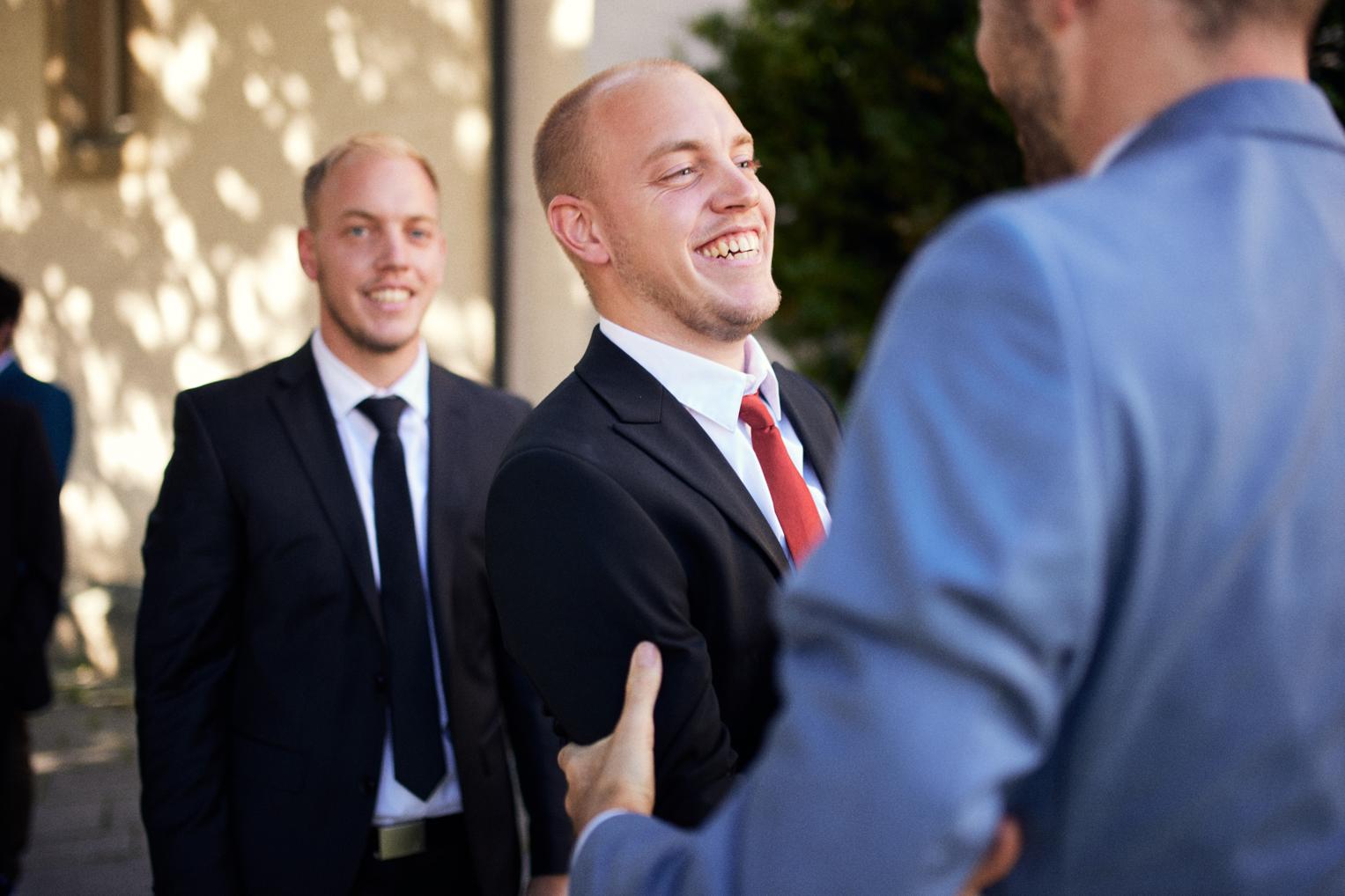 Männergäste lachen beim Sektempfang vor der Kirche Dettingen