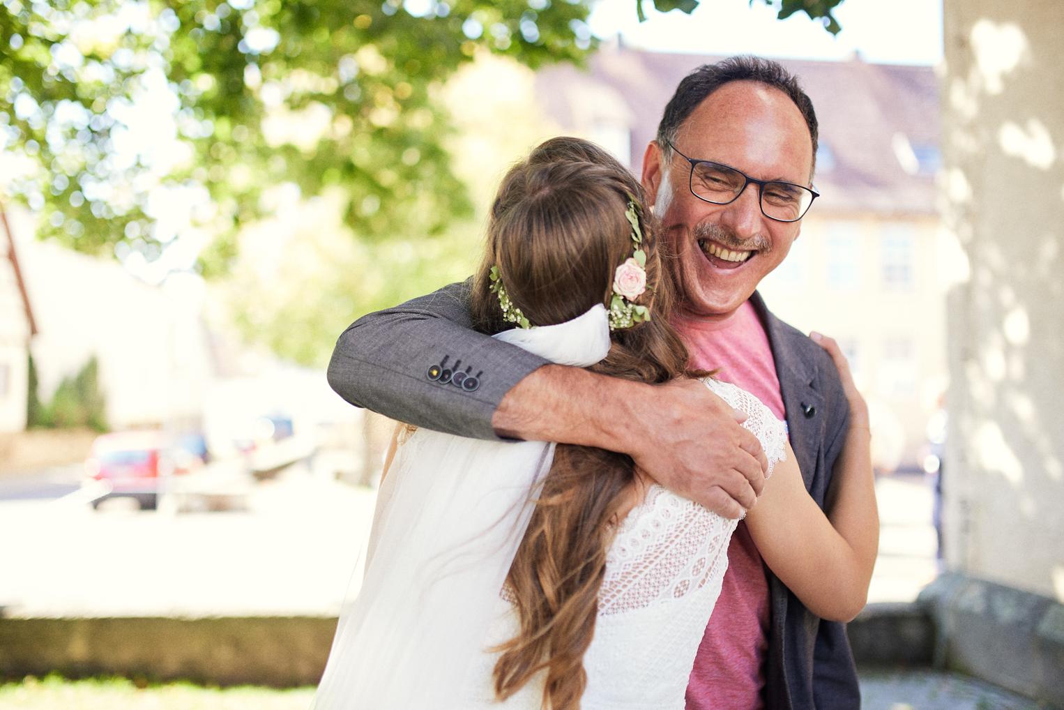 Vater umarmt seine Tochter lachend nach der kirchlichen Trauung