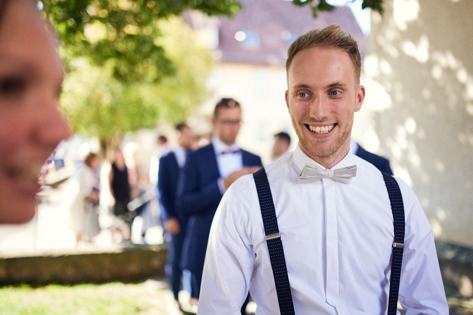 Junger Gast mit Hosenträgern lacht beim Sektempfang