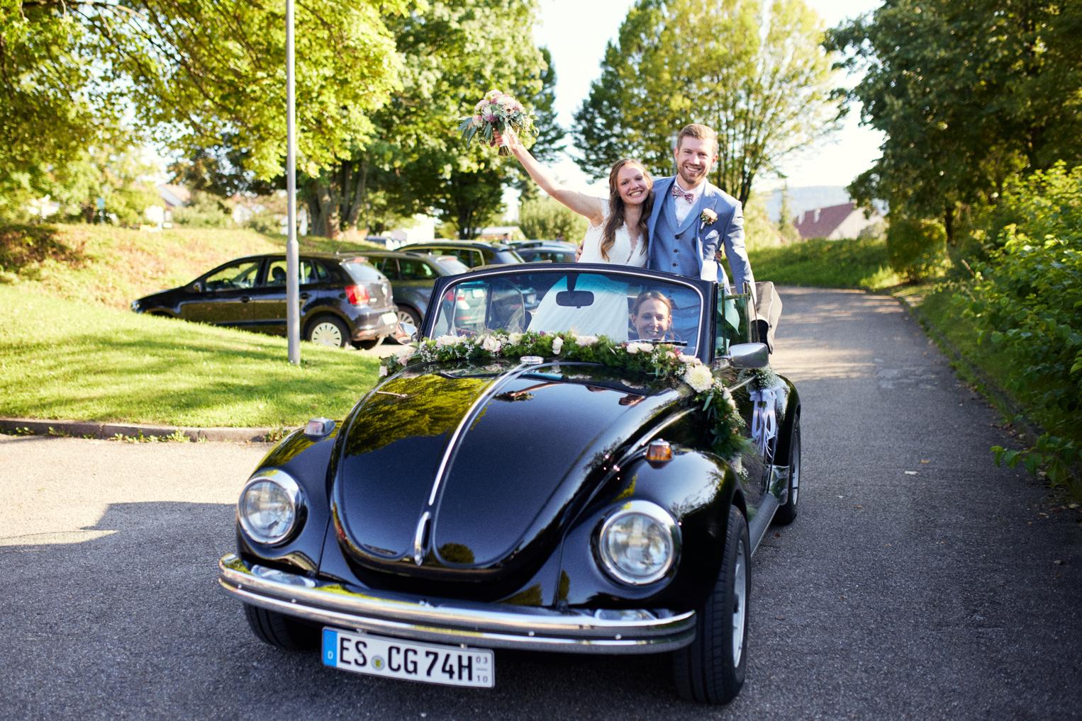 Brautpaar kommt im schwarzen VW Käfer Cabrio am Saal an