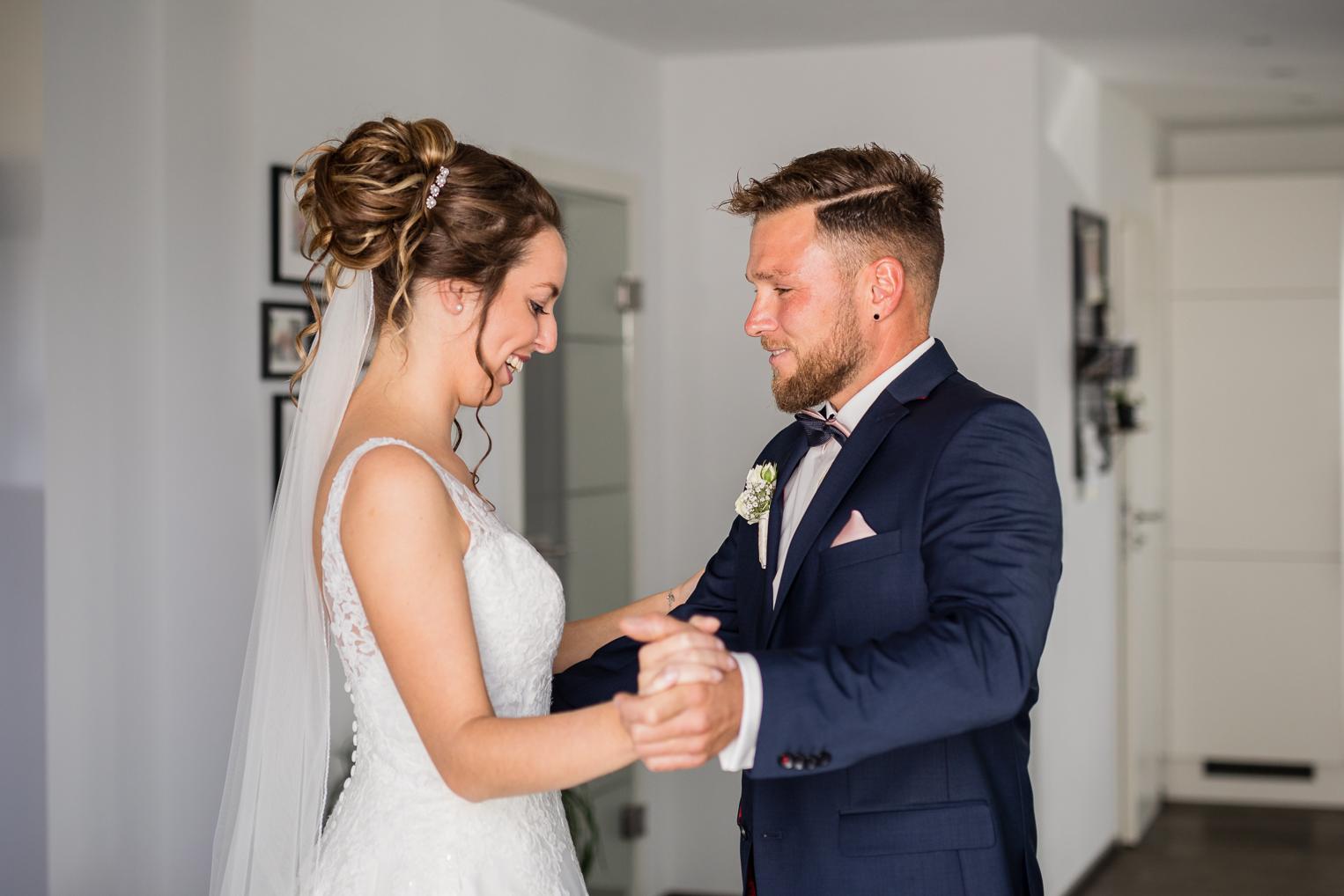First Look: Brautpaar hält sich an den Händen und lacht sich an, Getting Ready zuhause